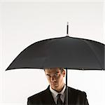 Caucasian mid-adult businessman  looking out at viewer from under umbrella.
