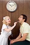 Caucasian mid-adult female nurse  examinating male's mouth with tongue depressor.