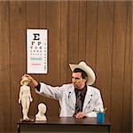 Mid-adult Caucasian male doctor wearing cowboy hat sitting at desk playing with figurine.