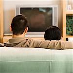 Asian couple sitting on couch watching TV.