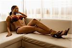Young African American woman reclining on couch in lingerie and heels.