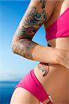 Tattooed woman in hot pink bikini with Pacific Ocean in background in Maui, Hawaii, USA.