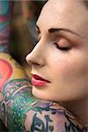 Close-up portrait of attractive woman's face and tattooed arm.