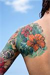 Close-up of Caucasian woman's back and shoulder covered with floral tattoos.