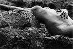 Young adult Caucasian female nude lying on rocky coast of Maui, Hawaii.