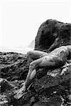 Young adult Caucasian female nude lying on rock in Maui.