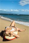 Sexy young Caucasian  woman in bikini lying on surfboard sunbathing at beach in Maui Hawaii.