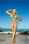 Pretty Caucasian mid adult woman bodybuilder in bikini flexing bicep on Maui beach.