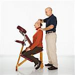 Caucasian middle-aged male massage therapist massaging neck of Caucasian middle-aged woman sitting in massage chair.