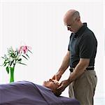 Caucasian middle-aged male massage therapist massaging face of Caucasian middle-aged woman lying on massage table.