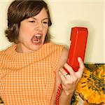 Pretty Caucasian mid-adult woman screaming at red telephone receiver.