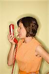 Pretty Caucasian mid-adult woman wearing orange dress sticking out tongue at red telephone receiver.