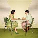 Caucasian mid-adult man and woman wearing vintage clothing sitting at 50's retro dinette set facing each other.