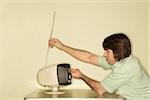 Side view of Caucasian mid-adult man sitting at 50's retro dinette set adjusting old television antenna.
