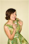 Pretty Caucasian mid-adult woman wearing green vintage dress with handheld radio smiling at viewer.