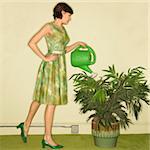 Pretty Caucasian mid-adult woman wearing vintage dress watering houseplant with green watering can.