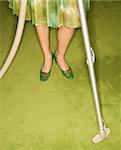 Close-up of Caucasian female legs with vacuum extension against green retro carpet.