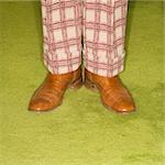 Close-up of Caucasian male legs in plaid pants standing on green retro carpet.
