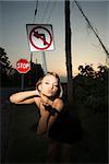 Caucasian mid-adult blonde woman wearing little black dress blowing kiss at viewer beside no left turn sign and stop sign.