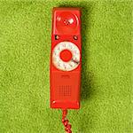 Red vintage rotary telephone receiver lying on 70's green carpet.