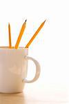 Three pencils in a coffee cup with pointed ends up.