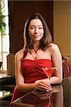 Taiwanese mid adult woman in red dress  at bar with a drink.