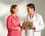 Asian American male doctor consulting with pregnant Caucasian woman.