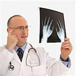 Caucasian mid adult male physician holding up hand xrays looking perplexed.