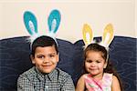 Hispanic brother and sister wearing bunny ears smiling and looking at viewer.