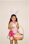 Hispanic girl wearing bunny ears holding Easter basket smiling and looking at viewer.