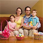 Caucasian family on couch holding Easter basket and looking at viewer.