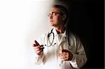 pensive doctor in glasses with stethoscope looking from the darkness to the light