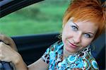 Young red-haired woman is siting in a car. Woman is happy