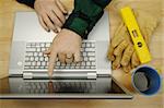 Contractor Reviews Project on Laptop with level, gloves and coffee to his side. Great image for online information regarding home improvement, additions, remodeling or construction.