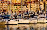 The Vieux Port (old port) in the city of Cannes in the French riviera, as the first rays of the morning sun illuminate the marina and the buildings behind the boats.