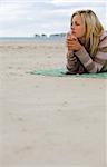 A beautiful blond haired blue eyed young woman laying alone on a beach deep in thought