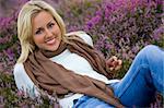 A beautiful blond haired blue eyed young woman laying amongst flowering heather and smiling