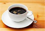 Closeup of black coffee in a white cup. Shot on light wood background