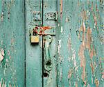 Rusty, unused lock on an old wooden door with peeling paint.