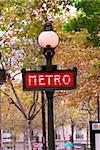 Red metro sign in Paris France on background of fall trees