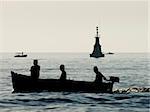 Calm atmosphere with small motor boat passing by at sunset. Focus on the back with lighthouse and second motor boat.