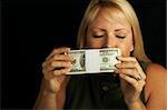 Attractive Woman Enjoys the Smell of Her Stack of Money on a Black Background