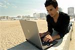 Attractive cool young man at the beach works with a notebook