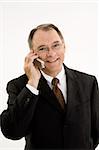 A caucasian businessman with a receding hairline wearing a gray business suit and white shirt. He is shown on a white background talking on a cell phone and is smiling.