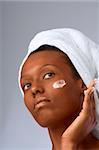 African-American girl applying facial skincare product (gray background )