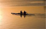 silhouette of people rowing a boat at sunrise.