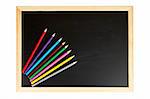 A empty black chalkboard with multicolored pencils. Path included