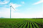 Wind turbine standing against a blue skywith some clouds in a green grass field