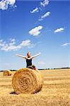 Woman enjoying the summer sun sitting on a hay bale under a bright blue sky