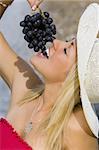 A beautiful young blond woman sitting in front of a fountain eating a bunch of black grapes